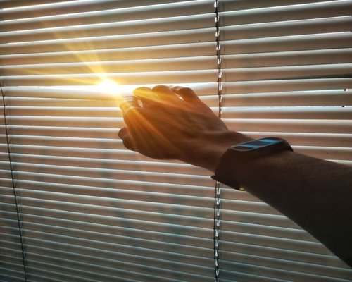 Person adjusting blinds on a window to control sunlight